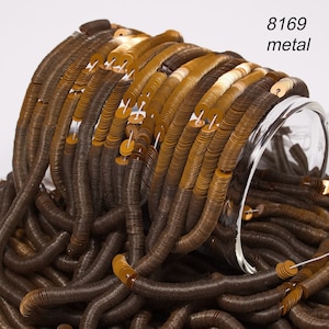 May include: A close-up of a pile of gold and brown metal sequins. The sequins are arranged in a circular pattern and are strung together on a thread. The sequins are in a glass jar. The text "8169 metal" is visible in the top right corner of the image.