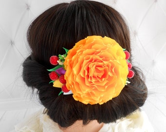 May include: A large orange flower hair clip with green leaves and red berries. The flower is made of fabric and has a ruffled texture.