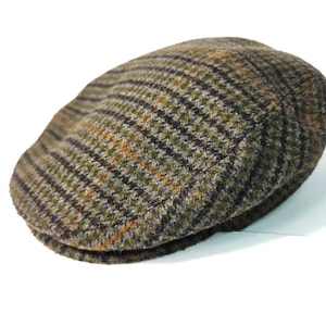 May include: A tweed flat cap in shades of green, brown, and black. The cap features a classic plaid pattern and a rounded, low-profile design. This hat is a stylish accessory for cooler weather.