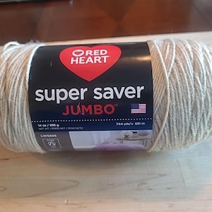 May include: A jumbo-sized skein of Red Heart Super Saver yarn in a neutral beige color. The label features a red heart logo and the text "Super Saver JUMBO". The yarn weighs 14 oz / 396 g and has 744 yds / 681 m.