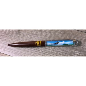 May include: A brown ballpoint pen featuring the yellow UPS logo on the barrel. The upper section is a clear, cylindrical chamber containing a floating graphic of a white airplane flying against a blue sky with clouds, finished with a silver cap.