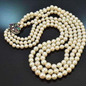 Pode incluir: Colar de pérolas de várias voltas com fecho decorativo. O fecho apresenta um conjunto de pedras preciosas coloridas, incluindo pedras vermelhas, verdes e azuis. As pérolas são de cor branco creme e estão dispostas em várias voltas.