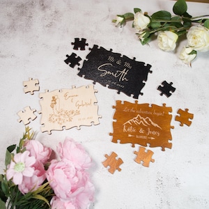 May include: Wooden jigsaw puzzles with personalized text for weddings. One is black with "Mr & Mrs Smith" and the date. Another is light wood with "Emma & Gabriel". The third is brown with "Katie & Jones".