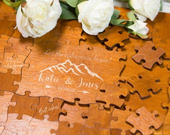 Könnte beinhalten: Ein Holzpuzzle mit personalisiertem Design, mit dem Text "Let the adventure begin!" und den Namen "Katie & Jones". Das Puzzle ist teilweise zusammengesetzt, mit mehreren verstreuten Teilen. Weiße Rosen sind auf dem Puzzle platziert.