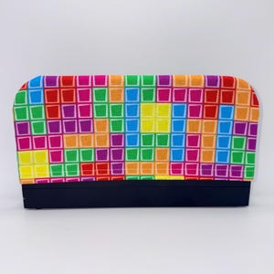 May include: A rectangular, fabric-covered item with a vibrant, multicolored square pattern in shades of red, orange, yellow, green, blue, and purple. The base is a solid black. The item is set against a white background.