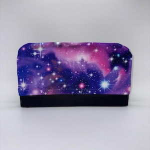 May include: A rectangular fabric item with a black base and a top featuring a vibrant galaxy design. The galaxy pattern includes shades of purple, pink, and blue, with numerous white and colored star-like accents.
