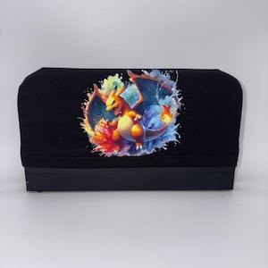 May include: Black console cover featuring a colorful graphic of a Charizard, a fire and dragon-type Pokémon. The artwork includes vibrant hues of orange, red, blue, and yellow. The cover is designed to fit a console.