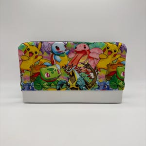 May include: A rectangular storage box featuring a colorful fabric cover with a repeating pattern of various cartoon creatures including yellow, green, and blue characters. The base of the box is a solid, smooth white plastic material.
