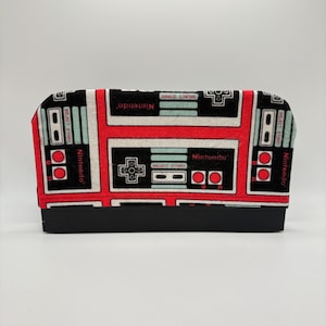 May include: A black and red Nintendo-themed case with a black base. The case features a repeating pattern of classic Nintendo controller designs, including the word "Nintendo" and the words "Select Start".