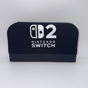 May include: Black Nintendo Switch console cover with white logo and text. The cover features the Nintendo Switch logo and the number 2, with the words "NINTENDO SWITCH" below. The cover is rectangular with rounded top edges.