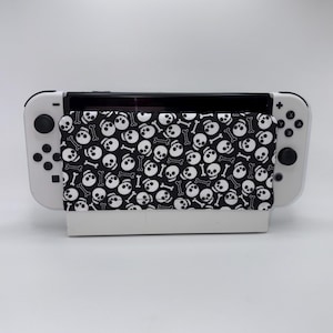May include: A white Nintendo Switch console with a black screen and white controllers. A black and white fabric cover with a skull and crossbones pattern is placed over the console.