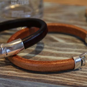 May include: Two leather bracelets with silver clasps. One bracelet is brown and the other is black.