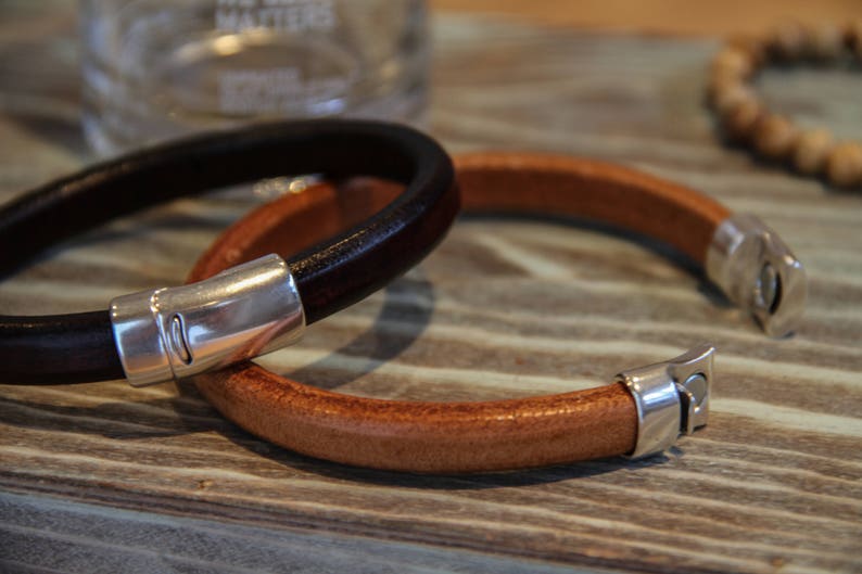 May include: Two leather bracelets with silver clasps. One bracelet is brown and the other is black.