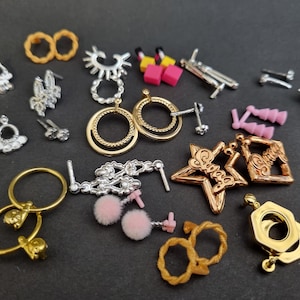 Puede incluir: Surtido de pendientes dorados, plateados y rosas, incluyendo pendientes en forma de estrella con la palabra "Sweet" en ellos, y un par de pendientes con diseño floral.