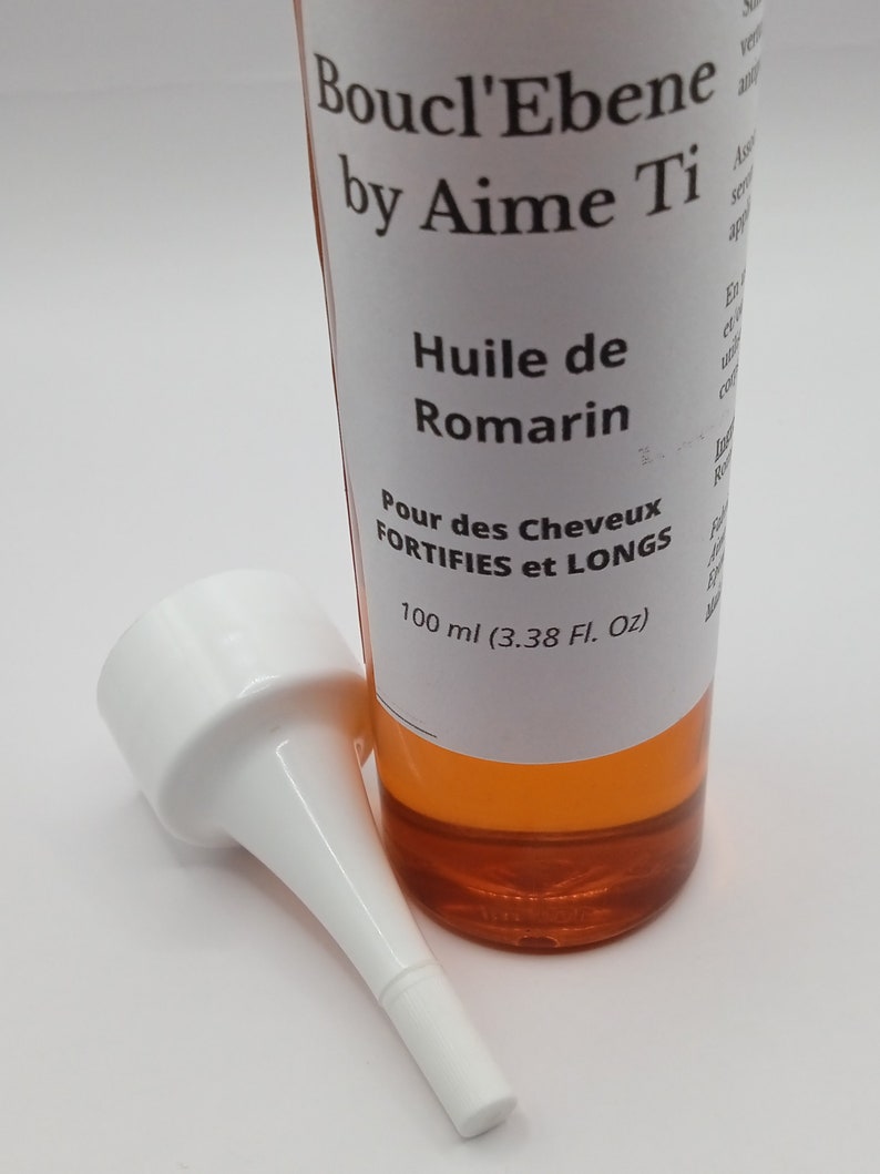 May include: A clear glass bottle with a white label that reads "Boucl'Ebene by Aime Ti Huile de Romarin Pour des Cheveux FORTIFIES et LONGS 100 ml (3.38 Fl. Oz)". The bottle contains a yellow liquid and has a white plastic applicator tip.