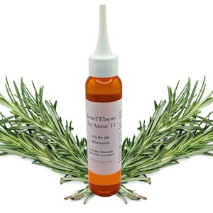 May include: A brown glass bottle with a white dropper top filled with a clear amber liquid. The bottle is labeled "Boucl'Ebene by Aime'Ti Huile de Romarin Pour des Cheveux Secs et Longs 100 ml (3.38 fl. oz)". The bottle is surrounded by sprigs of rosemary.
