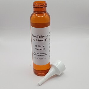 May include: A brown bottle with a white label that reads "Boucl'Ebene by Aime Ti Huile de Romarin Pour des Cheveux FORTIFIES et LONGS 100 ml (3.38 FL OZ)". The bottle has a white plastic tip attached to the top.