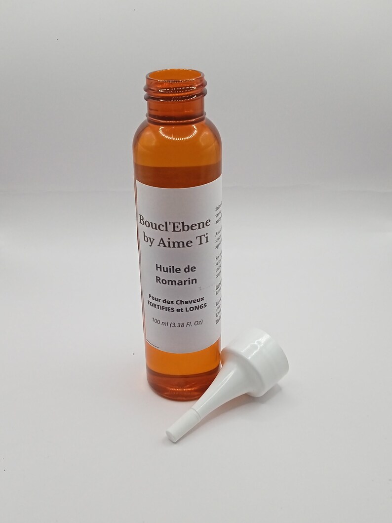 May include: A brown bottle with a white label that reads "Boucl'Ebene by Aime Ti Huile de Romarin Pour des Cheveux FORTIFIES et LONGS 100 ml (3.38 FL OZ)". The bottle has a white plastic tip attached to the top.