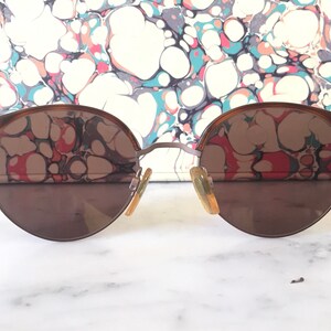 Puede incluir: Un par de gafas de sol redondas con montura marr&oacute;n y lentes marrones. Las gafas reflejan un patr&oacute;n de m&aacute;rmol.