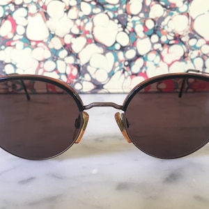 Puede incluir: Gafas de sol redondas marrones con montura de carey y detalles met&aacute;licos.