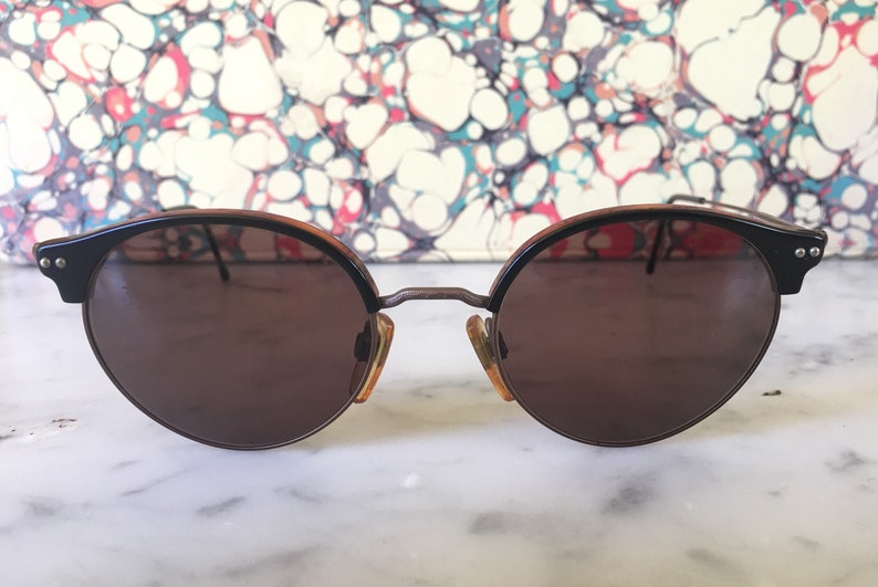 Puede incluir: Gafas de sol redondas marrones con montura de carey y detalles met&aacute;licos.