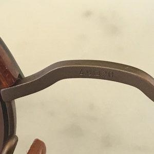 Puede incluir: Primer plano del brazo de metal marr&oacute;n de unas gafas de sol con el n&uacute;mero "49 20" grabado en el brazo.