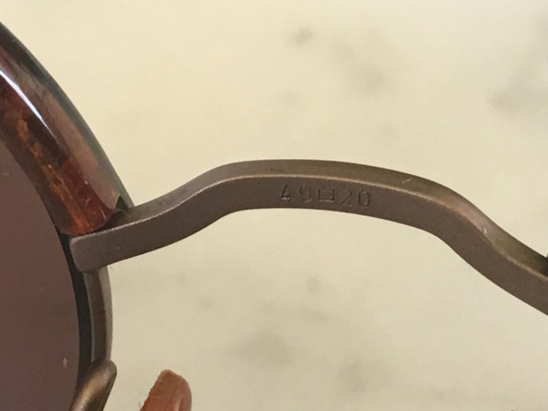 Puede incluir: Primer plano del brazo de metal marr&oacute;n de unas gafas de sol con el n&uacute;mero "49 20" grabado en el brazo.