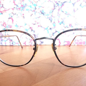 Puede incluir: Un par de gafas de pasta de carey con monturas redondas y finas varillas metálicas.