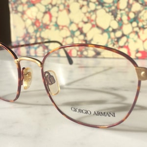 May include: A pair of tortoiseshell eyeglasses with gold accents and the brand name "Giorgio Armani" printed on the right lens.