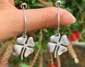 May include: Silver hoop earrings with a four-leaf clover charm hanging from each hoop.