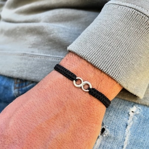 Puede incluir: Un brazalete de cuerda negro con un dije de plata en forma de infinito.