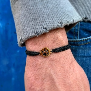 May include: A black braided bracelet with a gold paw print charm.