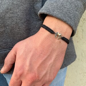 May include: A black braided bracelet with a silver angel wing charm.