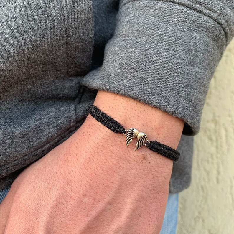 May include: A black braided bracelet with a silver wing charm.