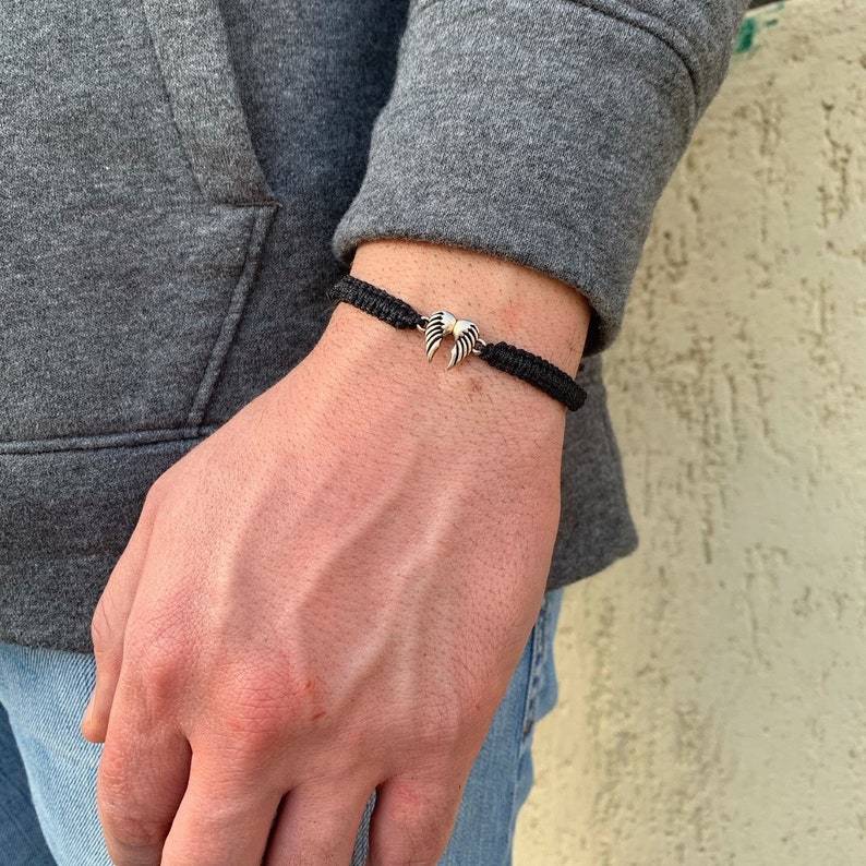May include: A black braided bracelet with a silver wing charm.