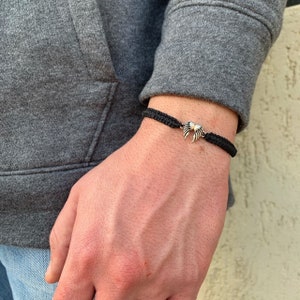 May include: A black braided bracelet with a silver angel wing charm.