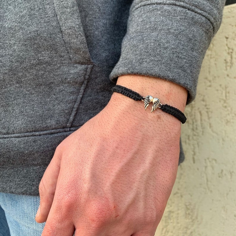 May include: A black braided bracelet with a silver angel wing charm.