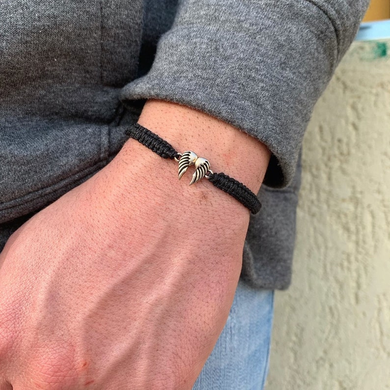 May include: A black braided bracelet with a silver wing charm.