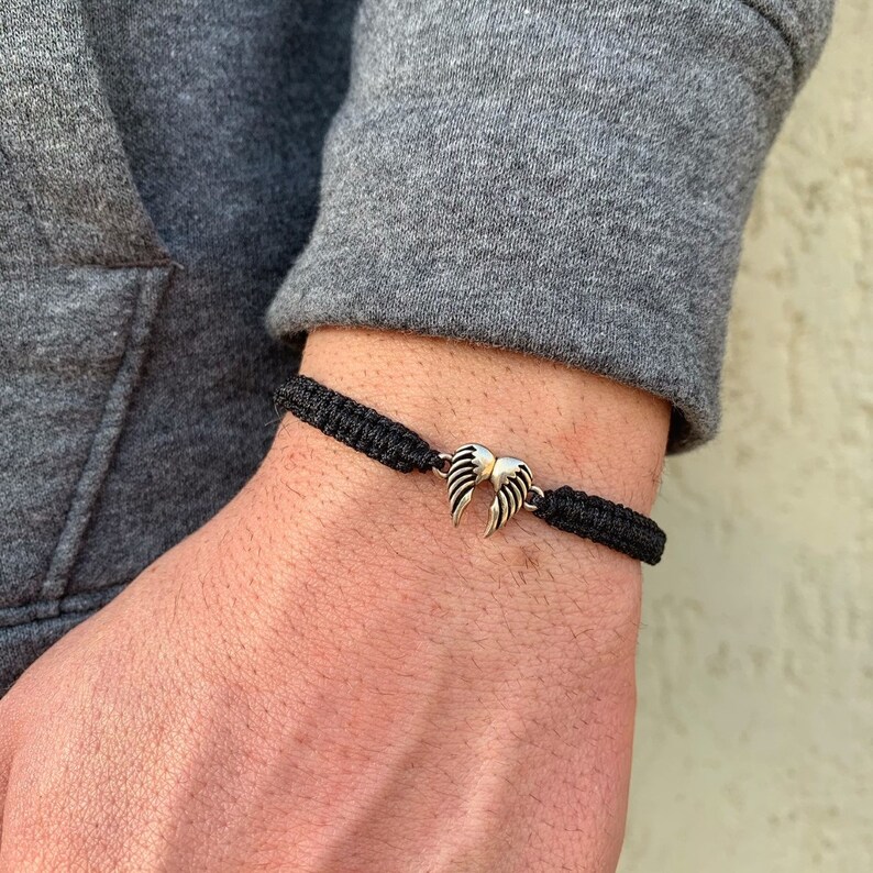 May include: A black braided bracelet with a silver angel wing charm.