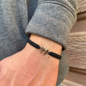 May include: A black braided bracelet with a gold-toned angel wing charm.