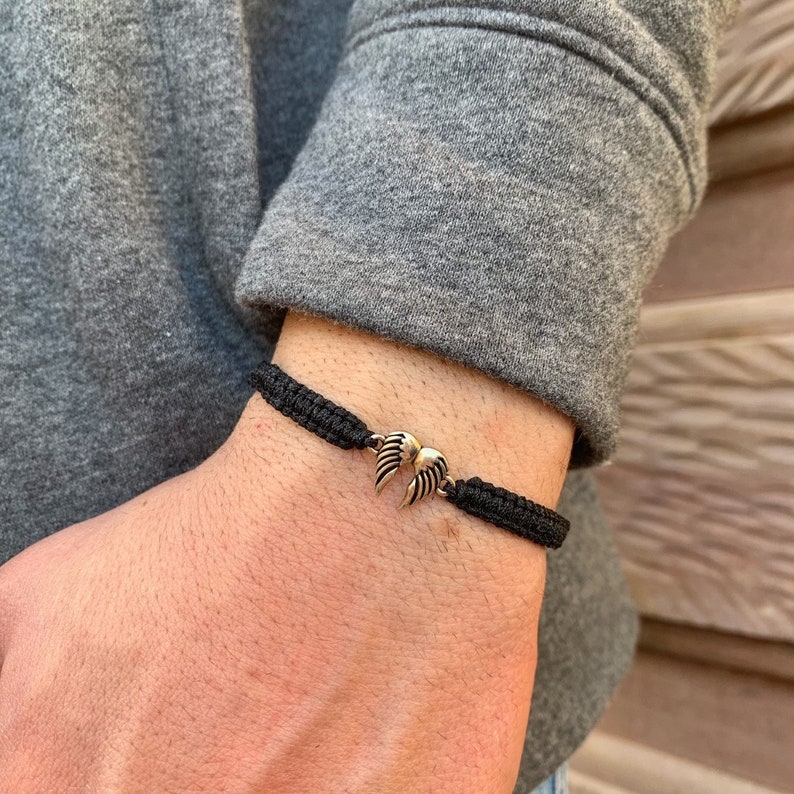 May include: A black braided bracelet with a gold-toned angel wing charm.