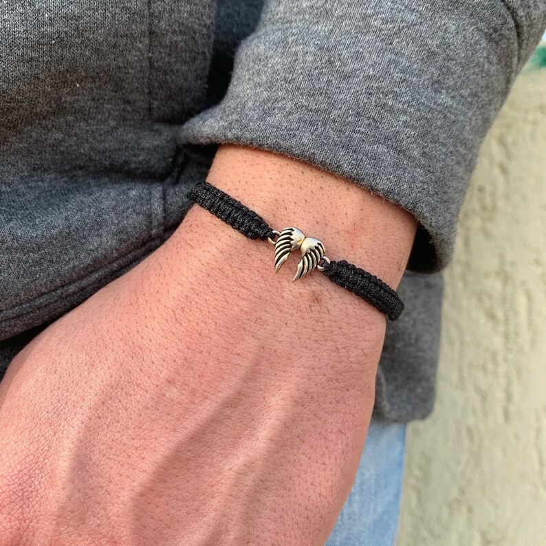 May include: A black braided bracelet with a silver angel wing charm.