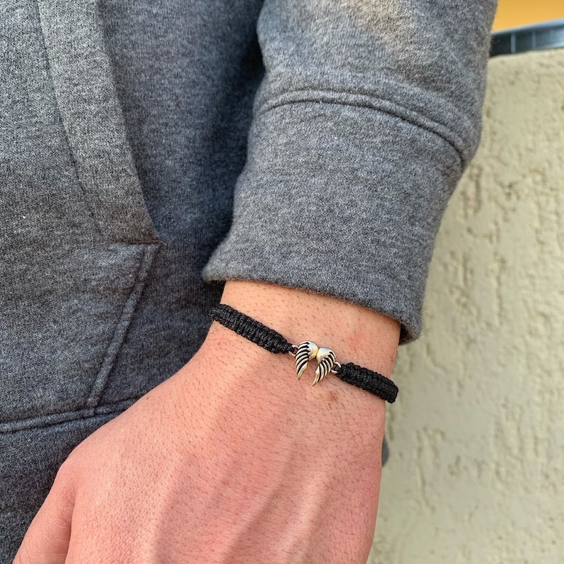 May include: A black braided bracelet with a silver wing charm.