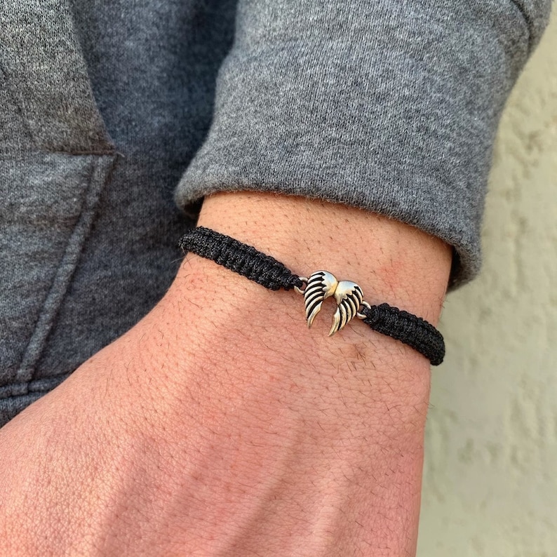 May include: A black braided bracelet with a silver angel wing charm.