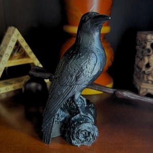 Pode incluir: Uma vela de corvo preto com penas detalhadas e um design realista. A vela está empoleirada em uma base de galho de árvore.