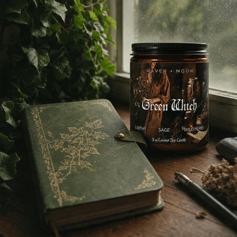 May include: An 8 oz coconut soy candle in a brown glass jar with a black lid. The label features the text Maven + Moon, Green Witch, Earthy, Sage, and Wild Herbs, alongside an illustration of a person holding herbs and glass apothecary bottles.