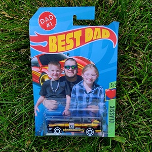 May include: A Hot Wheels toy car in a package with the words "BEST DAD" and "DAD #1". The car is black, yellow, and red with the number 84 on the side. The package has a photo of a man and two children.