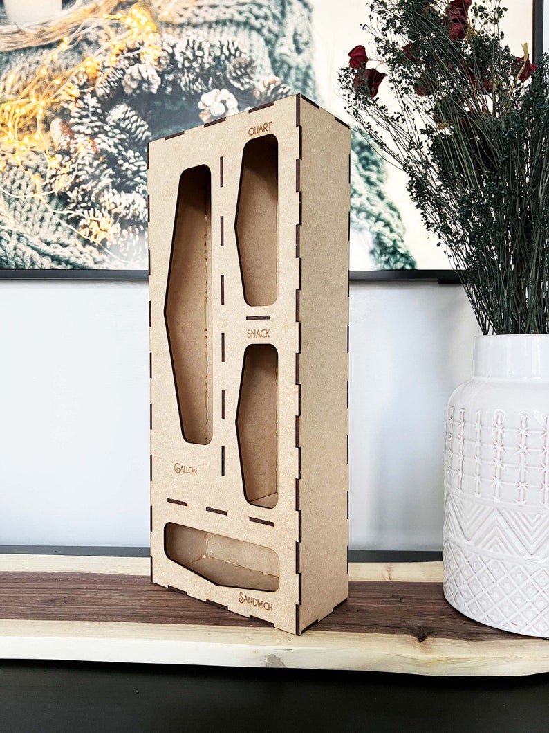 May include: A wooden organizer with four compartments for storing different sizes of containers. The compartments are labeled "Gallon", "Snack", "Quart", and "Sandwich".