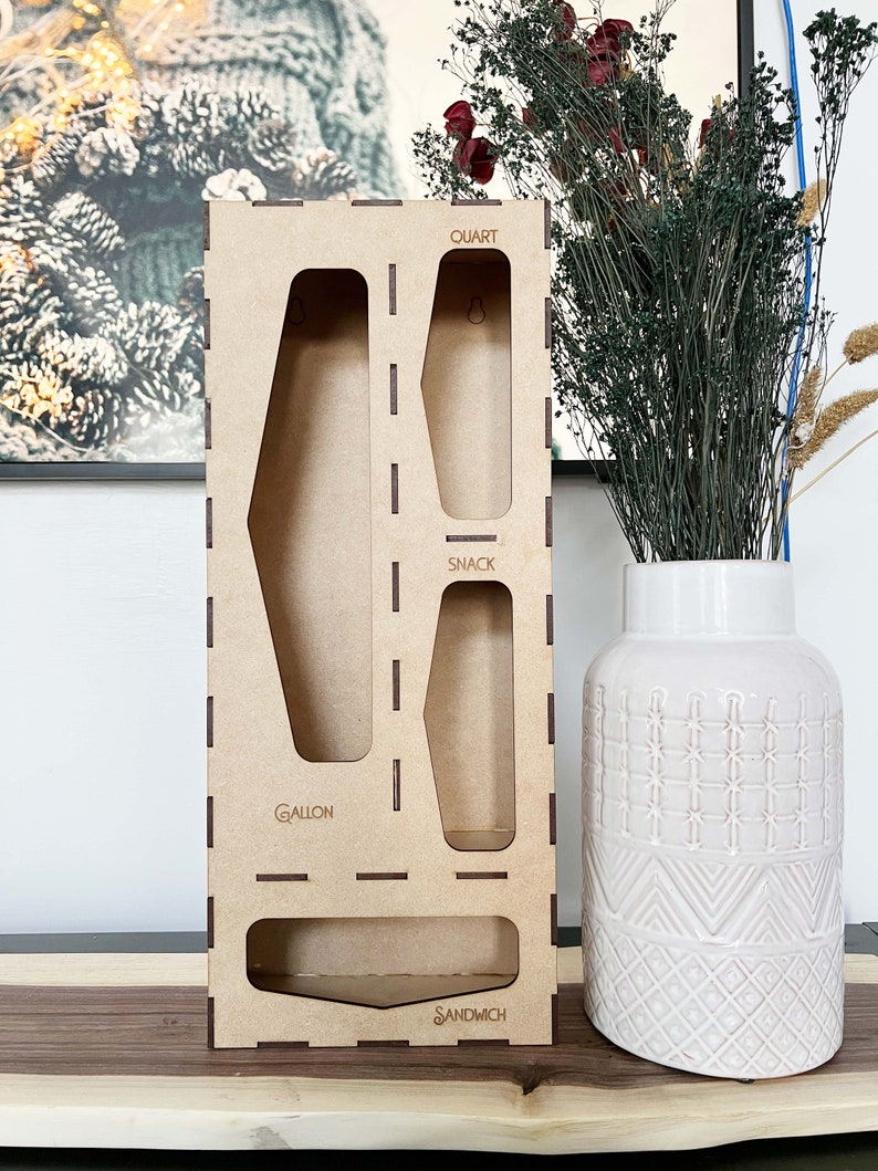 May include: A wooden organizer with four compartments for storing different sized containers. The compartments are labeled "Gallon", "Snack", "Quart", and "Sandwich".