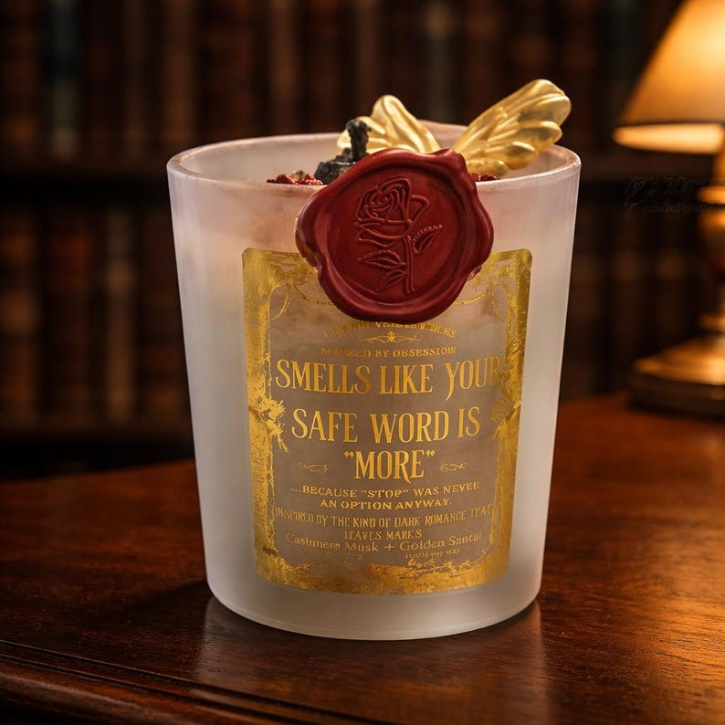 "Smells Like your safe word is "More"" 
Dark romance soy candle in matte white vessel with crimson wax bloom, golden wings, and gold foil label - Smells Like Your Safe Word Is More from Marked by Obsession collection